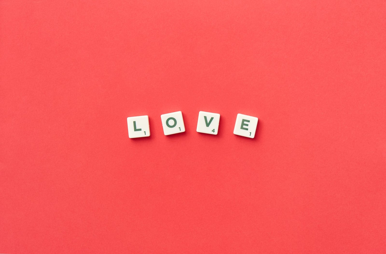 Scrabble tiles spelling "LOVE" on a vibrant red background, viewed from above, perfect for romantic themes.