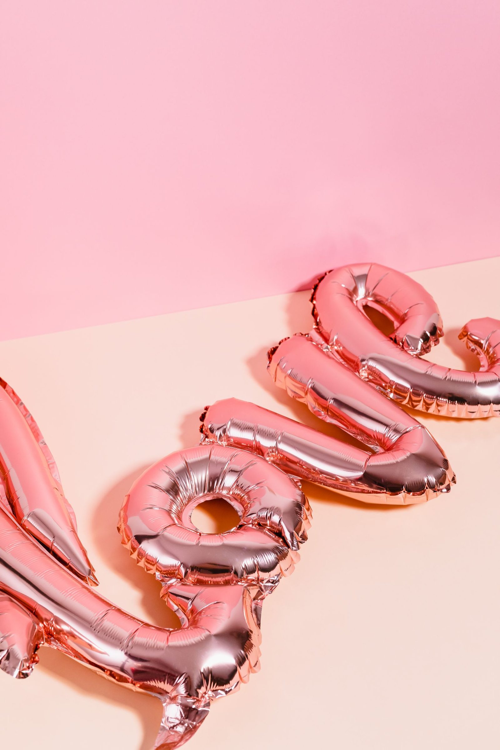 Shiny pink balloons spelling love on a pastel pink background, perfect for Valentine's Day or celebrations.