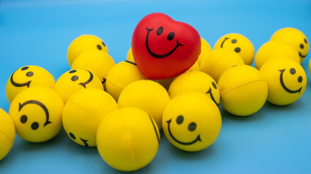 Bright yellow smiley face balls with a standout red heart-shaped ball on a blue surface.